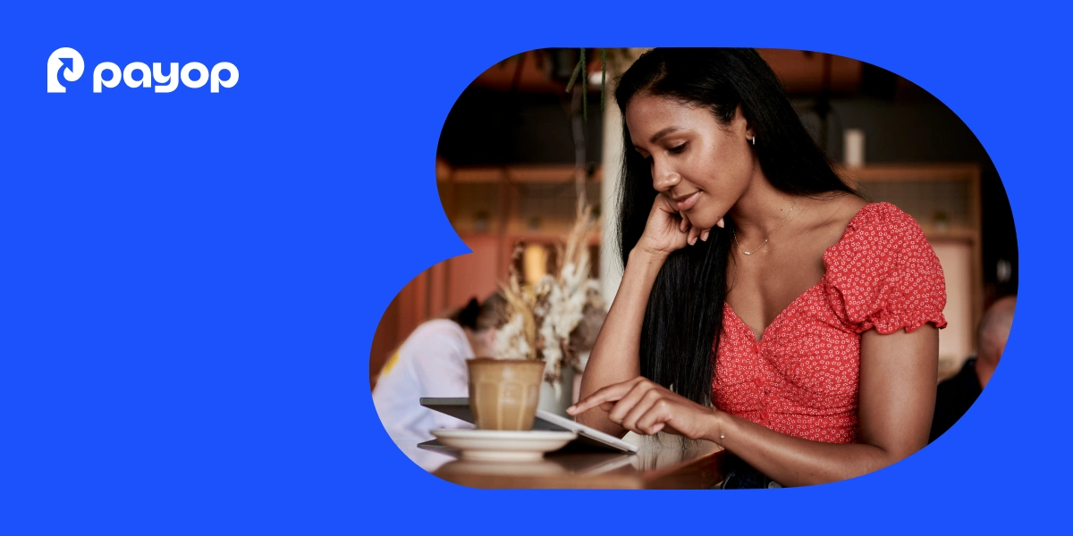 A woman in a red top smiles while using a tablet at a café, with a latte nearby. The atmosphere is relaxed and warm. Payop logo in the corner.