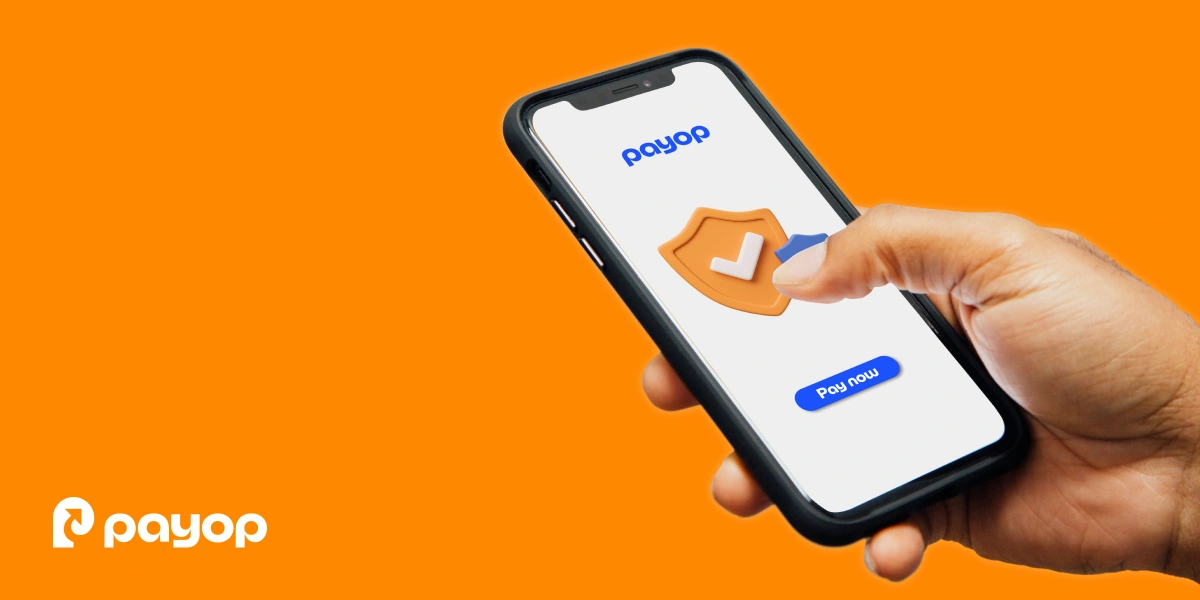 A hand holds a smartphone displaying a security icon and a "Pay now" button. The background is bright orange with the Payop logo.