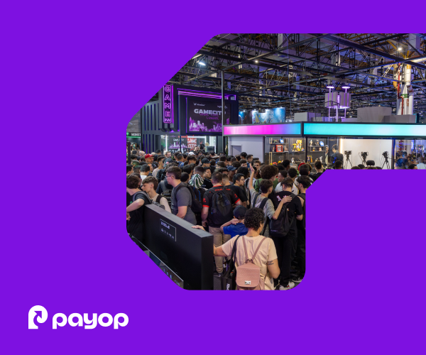 A filled exhibition hall with high ceilings, lighting trusses, and gaming booths. A large crowd of visitors fills the foreground. In the bottom-left corner, the white Payop logo. The image is framed within a graphical element on a purple background.