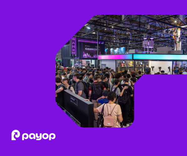 A filled exhibition hall with high ceilings, lighting trusses, and gaming booths. A large crowd of visitors fills the foreground. In the bottom-left corner, the white Payop logo. The image is framed within a graphical element on a purple background.