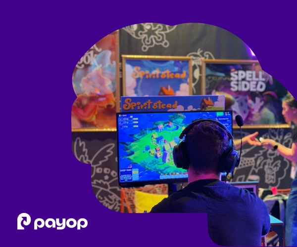 A gamer from behind, wearing headphones, looks at a computer screen showing a colorful game, within a purple frame featuring the Payop logo.